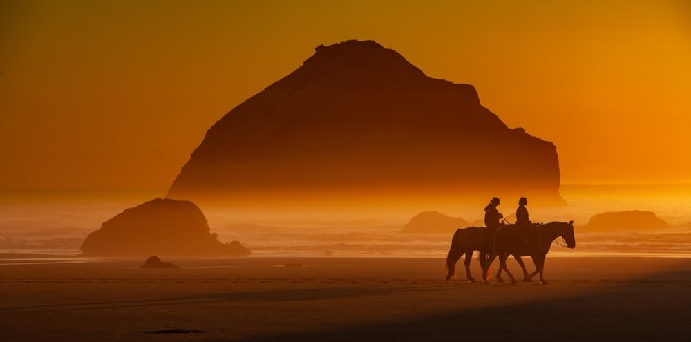 Oregon Getaways for Couples, photo of a couple horseback riding on the beach
